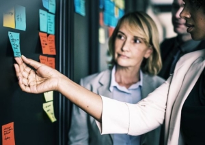 Two women review sticky notes on board